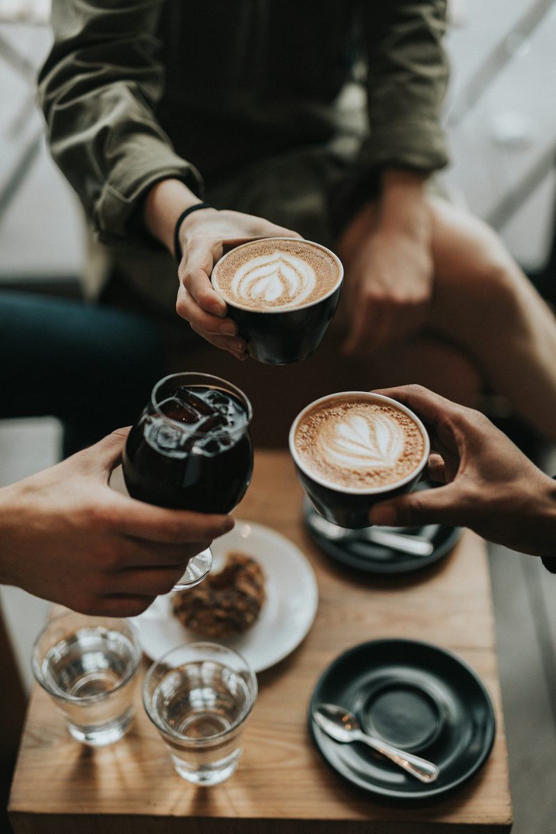 Friends clinking lattes over a table with pastries
