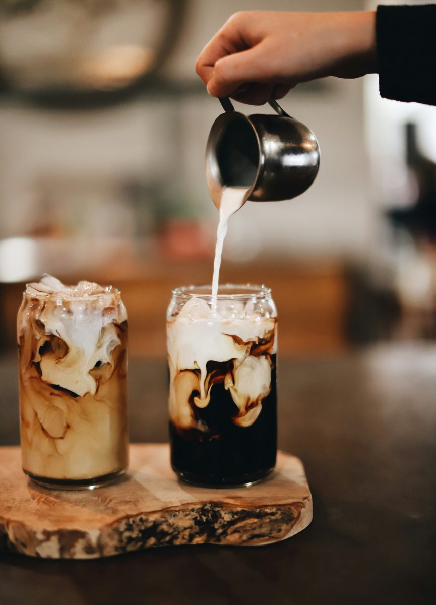 Two iced coffees with swirling cream on a wooden board